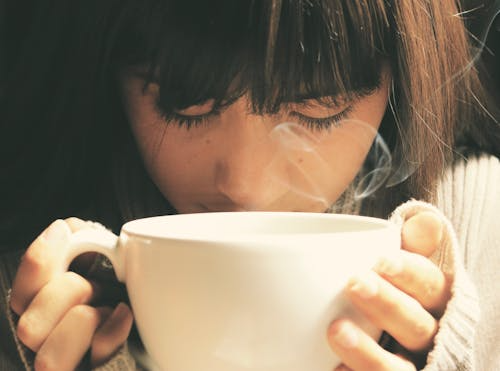 An image of a woman smelling the aroma of her chai in a cup