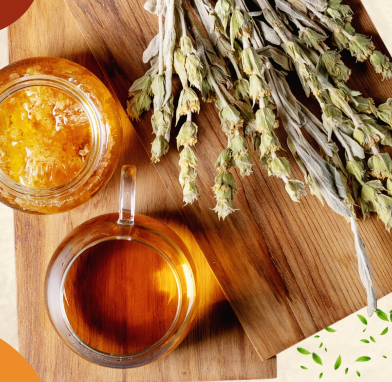 A glass cup of Greek mountain tea with a jar of honey and dried Sideritis herbs on a wooden board.
