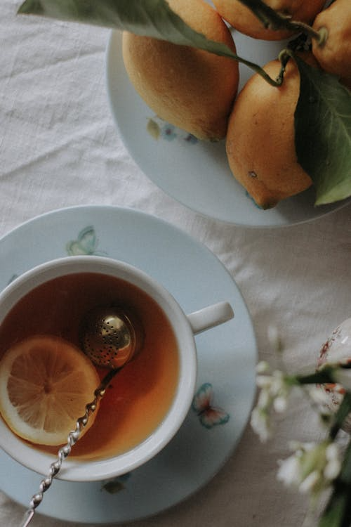 Glass mug of fruit tea with a gold spoon placed beside it on a white background