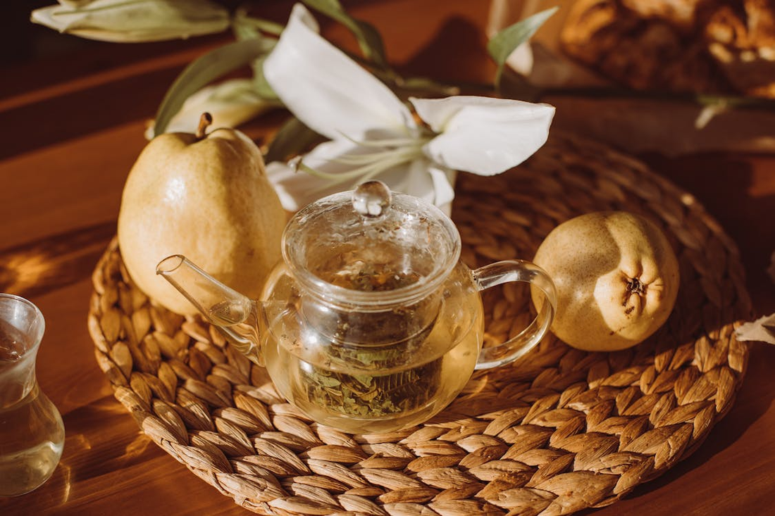Teapot beside a pear with caffeine-free fruit tea served in a glass cup.