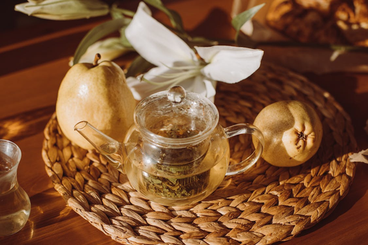 Teapot beside a pear with caffeine-free fruit tea served in a glass cup.