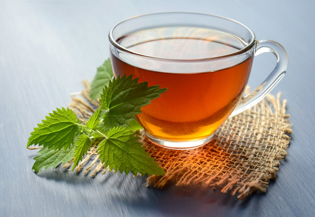 Clear glass cup of amber herbal tea with fresh green leaves resting on a burlap mat.