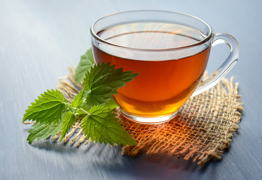 Clear glass cup of amber herbal tea with fresh green leaves resting on a burlap mat.