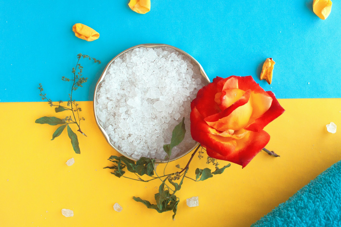 Flake salt in a bowl with rose petals and herbs on a colorful background.