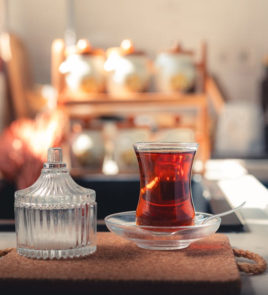 Clear glass mug with light-colored tea beside a linen napkin and wooden tray.