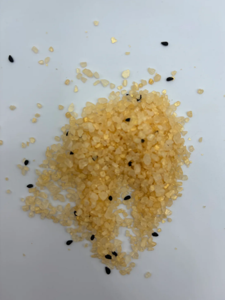 A close-up of golden salt crystals mixed with small black seeds scattered on a white surface.
