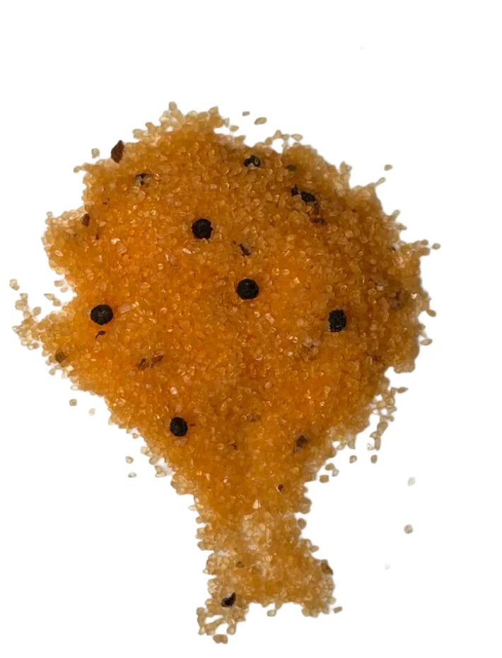 Close-up of vibrant orange seasoned salt with visible peppercorns, highlighting the texture and mineral-rich geometry of gourmet salts.