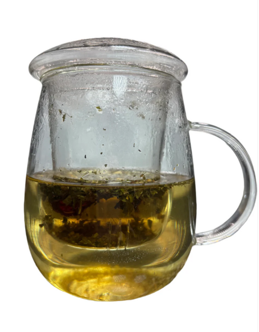 Glass mug of brewed Greek mountain tea with loose herbs visible in the infusion.