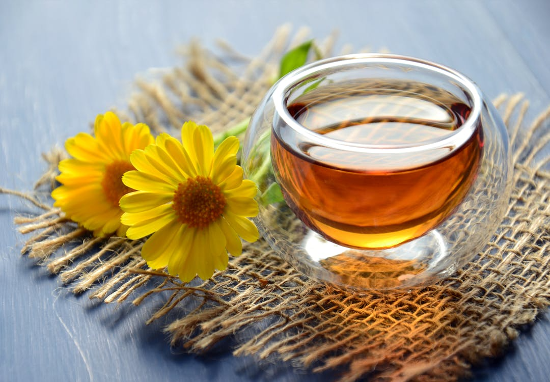Clear glass cup of green tea placed on burlap fabric with yellow flowers beside it
