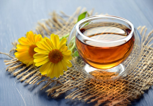 Clear glass cup of green tea placed on burlap fabric with yellow flowers beside it