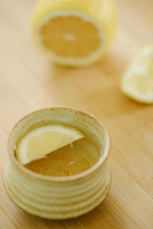 A small ceramic cup filled with herbal tea and a slice of lemon on a wooden surface.