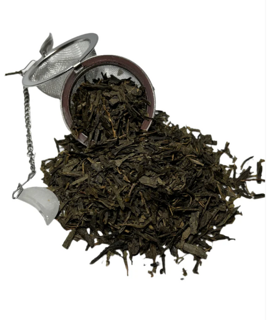 Loose green tea leaves spilling from a metal tea infuser on a white background.