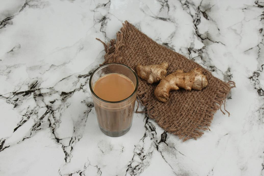 A cup of masala chai with fresh ginger and spices placed on a marble surface.