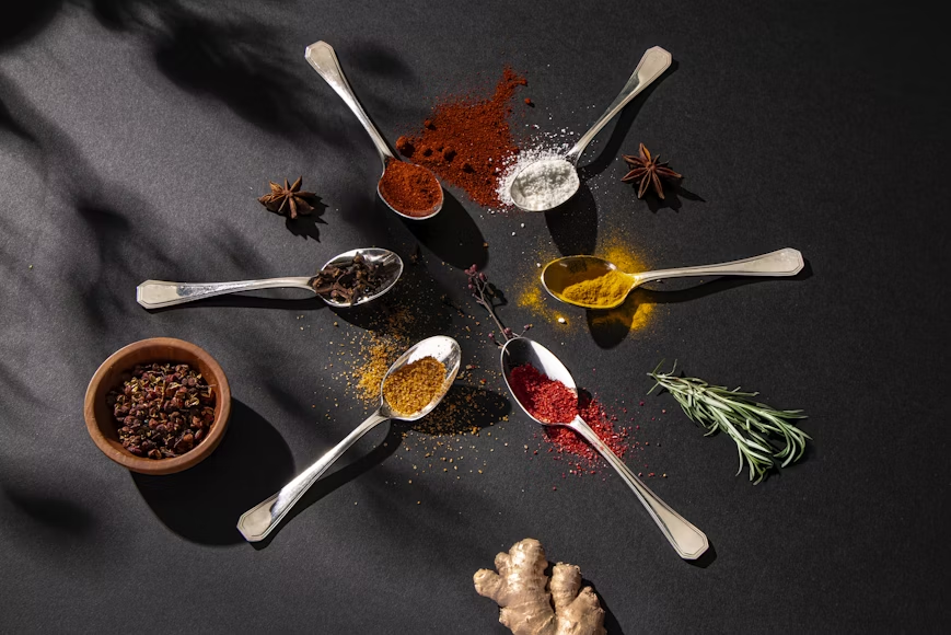Aesthetic image of spoons of spices placed on a black surface in a circle.