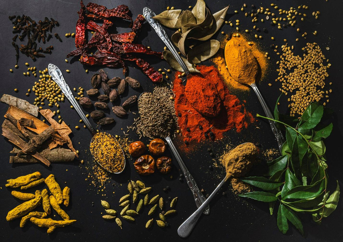 Flat lay image of scattered spices, herbs, and spoons with heaps of spice blends.
