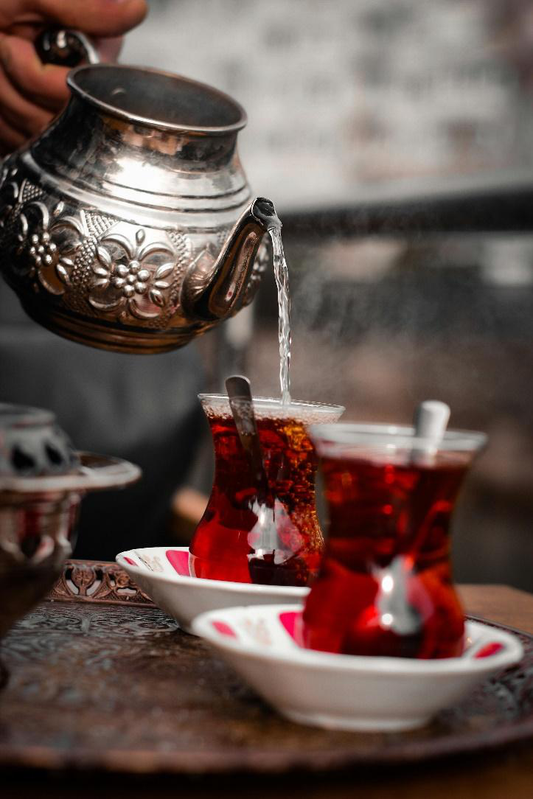 A person pouring freshly brewed rooibos tea into a cup, showcasing its rich amber color.