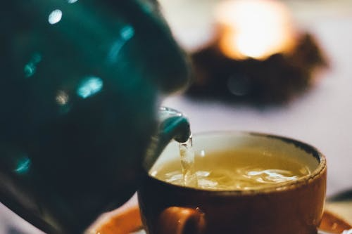 Person pouring brewed tea into a brown ceramic cup