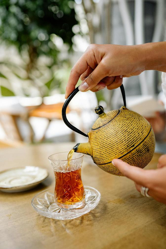 A person pouring freshly brewed loose leaf tea into a cup.