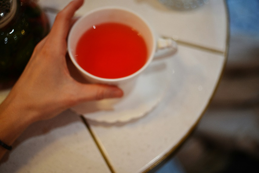 Cup of red rooibos tea held by hand on a white saucer.
