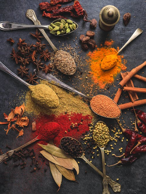 Assorted gourmet spices displayed in spoons on a table.