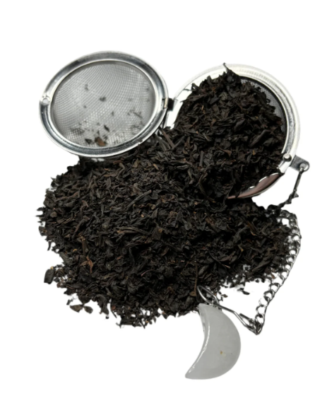 Loose black tea leaves spilling from a metal tea infuser with a crescent-shaped charm.