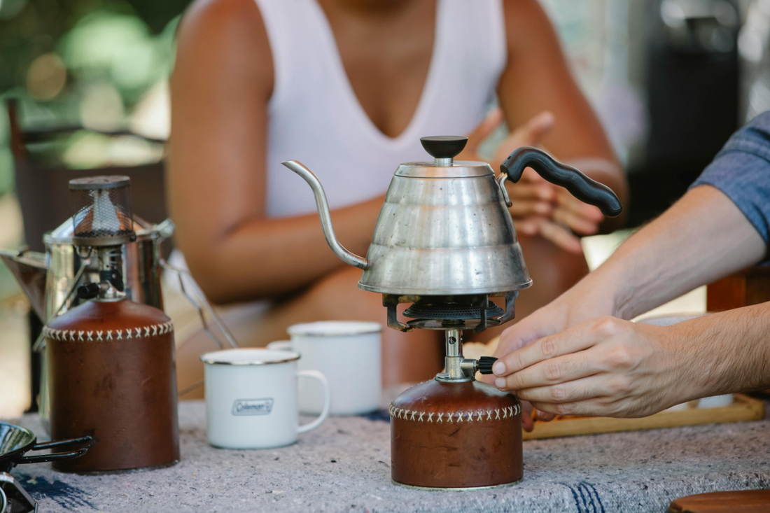 Couple heating a metal kettle on a camp stove outdoors, enjoying a cozy tea moment