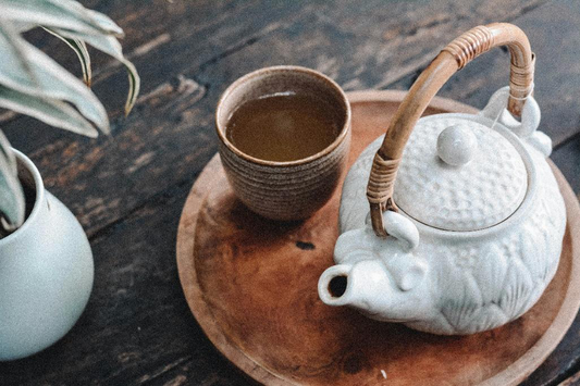 Ceramic teapot and cup of tea on a wooden tray.