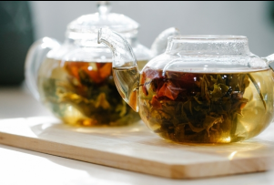 Two glass teapots with blooming tea flowers inside are set on a wooden board.