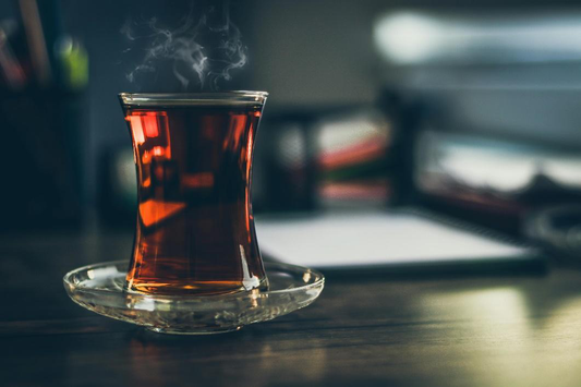 A steaming glass of dark amber black tea in a clear glass on a saucer.