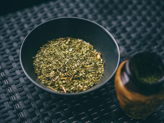 A black bowl filled with yerba mate set on a woven dark surface.